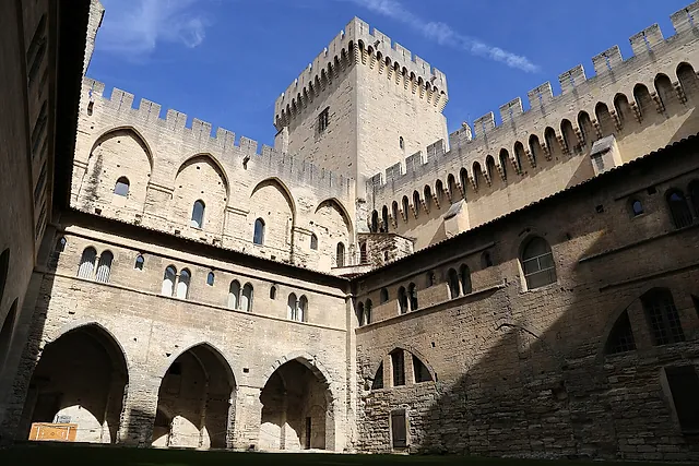 The cloister court of Benedict XII in the Palais des Papes: pointed arcades below crenellated walls and a tower