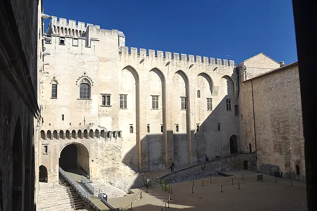 The Cour d'honneur of the Palais des Papes, with its tall crenellated walls and pointed arches in the sun