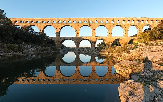 The Pont du Gard in warm evening light, its tiers of arches reflected in the river