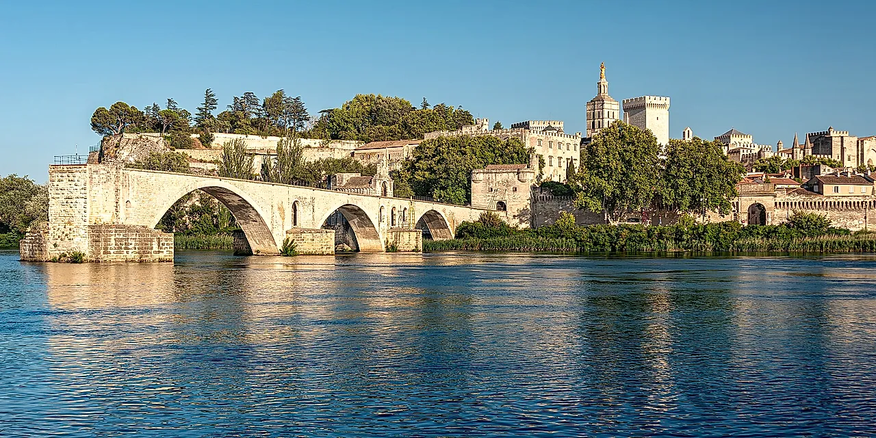 The arches of the Pont d'Avignon above the Rhône in golden light, with the Palais des Papes and the cathedral on the hill behind