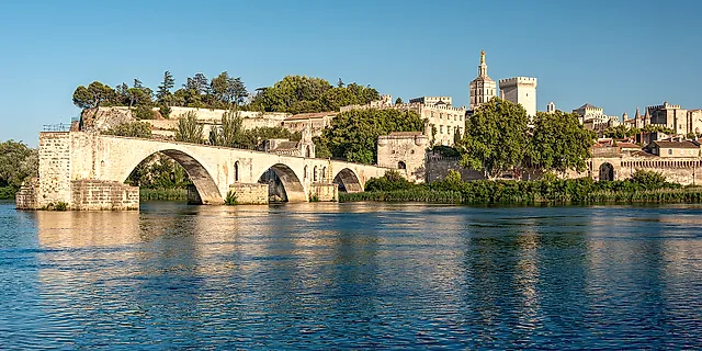 The arches of the Pont d'Avignon above the Rhône in golden light, with the Palais des Papes and the cathedral on the hill behind